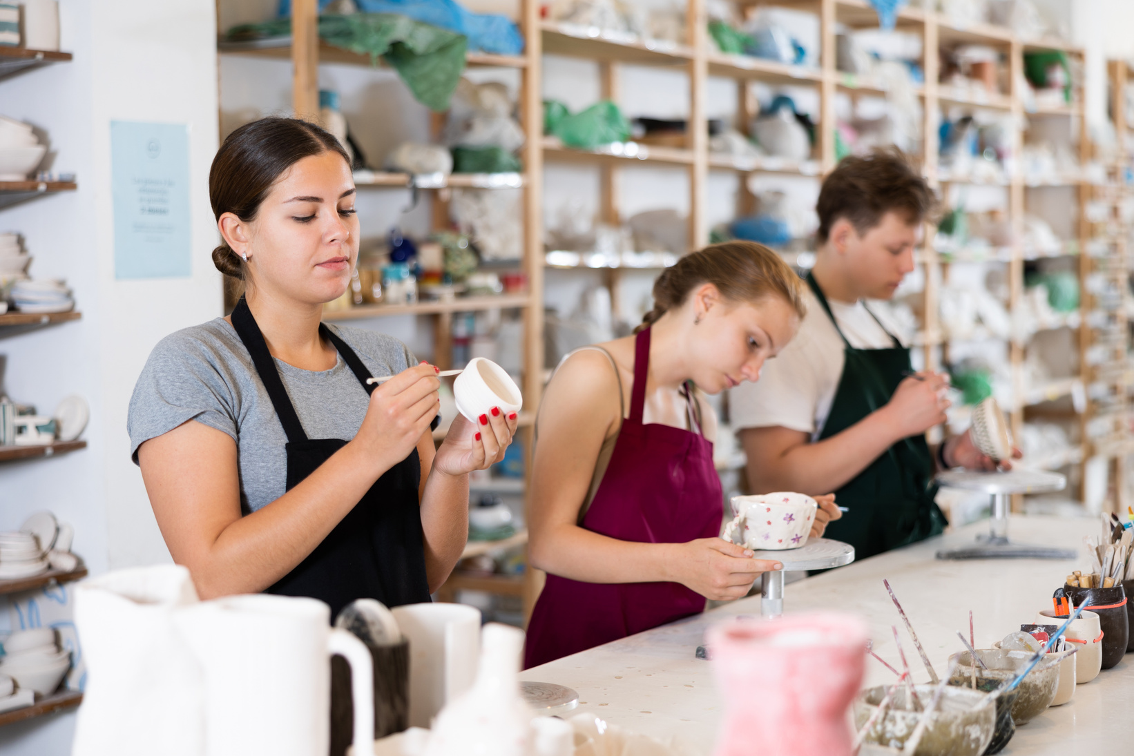 Young woman painting ceramic cup in ceramic workshop